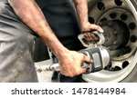 Small photo of Auto mechanic using industrial impact wrench to unbolt semi truck wheel