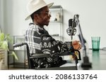 Side view portrait of African-American person with disability giving interview while recording podcast in studio