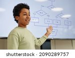 Portrait of smiling teenage boy giving presentation in coding class for children and pointing at digital screen, copy space