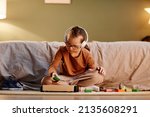 Small photo of Portrait of young girl with down syndrome playing with toy blocks alone and wearing noise cancelling earphones, overstimulation concept, copy space