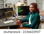 Portrait of female IT developer looking at camera and smiling against programming code on computer screen in office interior, copy space
