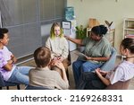 Group of teenagers sitting on chairs and talking their problems to psychologist who listening to them and giving advice during psychology therapy group