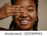 Close up portrait of ethnic young woman smiling candidly with one eye closed, skin texture acne scars