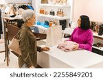 Portrait of smiling young woman working in clothing boutique and greeting senior customer