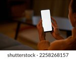 Young woman holding smartphone with white screen at home while relaxing in dark, copy space
