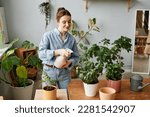 Portrait of smiling young woman watering plants indoors and caring for home greenery, copy space