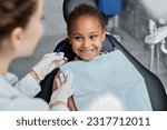 Portrait of smiling little girl in dental chair with nurse preparing her for teeth check up, copy space