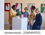 Small photo of Diverse group of teenagers listening to teacher or tour guide in modern art gallery or museum