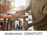 Small photo of Closeup of black black man polishing old furniture piece in restoration workshop lit by sunlight, copy space
