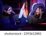 Side view portrait of two young women playing video games together and high five celebrating victory in cybersports club