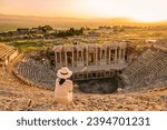 Small photo of Hierapolis ancient city Pamukkale Turkey, a young woman with a hat watching the sunset by the ruins Unesco Heritage. Asian women watching the sunset at the old Amphitheater in Turkey during holiday