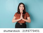 Smiling young Asian woman gesturing traditional greeting isolated over blue background