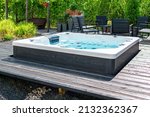 Small photo of Large hot tub embedded in the backyard terrace. A sunny summer's day in the shelter of a green garden. Everyday luxury and relaxation in your own backyard. Spa complex, vacation and traveling concept.