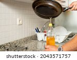 Small photo of Man placing recycled edible oil from a frying pan into a plastic bottle in his home kitchen. Recycle at home concept. High quality photo