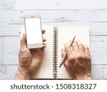 Hand with smartphone and silver pen on blank page diary top view space business concept