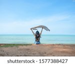 Small photo of Travel woman sit relax at the beach and show scarf up and blue ocean blue sky beautiful landscape,Travel and relax at the beach on holiday concept