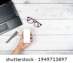 Top view workspace laptop glasses and two silver pen and hand hold smartphone white screen copy space