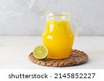 Freshly squeezed orange juice with ice and lime slices in a jug on the table.