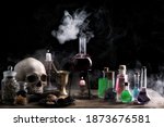 Small photo of Magic and wizardry concept. Magic potions, skull,books and candles on table. Potion with vapor streaming from bottle. Witch's house.