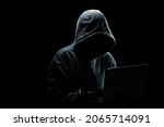 Hacker without a face in a hood on with laptop in the dark.