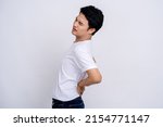 Small photo of Spine problems. Portrait of young asian man in casual white t-shirt holding his back, having sudden lower back pain, pinched nerve or kidney inflammation.
