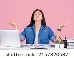 Small photo of Asian business woman wear casual shirt sit work at white office desk with pc laptop isolated on pastel pink background studio. She is hold hands in yoga om gesture relax meditate try to calm down.