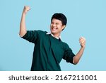 Small photo of Portrait of a cheerful young Asian man in casual clothes. He raised his fist with a happy smile on his face as a gesture of celebration.