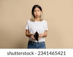 Small photo of I'm poor. Portrait of a sad Asian girl bankrupt and showing empty wallet and looking at camera.