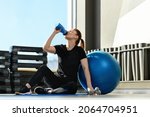 Woman with the Exercise Ball, drinks water from a bottle in the gym. Middle-aged  Fitness Woman. Sport and healthy lifestyle concepts