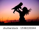 Silhouette happy mother and baby. Mother plays with her baby in her arms under the rays of the sunset in a meadow. Motherhood concept. Happiness, inspiring, joyful moments. Mother's day concept.
