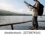 Man traveler holding map standing near lake with admiring picturesque scenery of mountainous. 