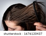 Young woman combing dirty greasy hair on gray background. 