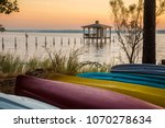 A lone brown pelicanon a post at sunset with colorful canoes on the shore of Mobile Bay, at Fairhope Alabama