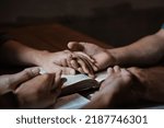 Small photo of A group of young Christians holding hands in prayer for faith and scriptures on a wooden table as they pray to God.