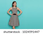 Charming fashion model in striped dress posing with hands on hip and looking away. Three quarter length studio shot on turquoise background.