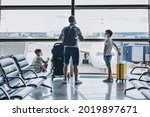 Father and sons in protective medical face mask with yellow suitcase at empty airport. Children looking out window at airplane. Family waiting for departure gate. Family trip and vacation concept.
