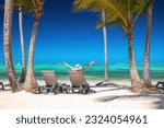 Exotic island beach with palm trees and sun lounges on the Caribbean Sea shore, summer tropical vacation.