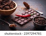 Small photo of Dark chocolate bar, red hot chilli pepper cayenne, dry hot chili spices, cocoa beans nibs powder, food tasty design on black wooden background