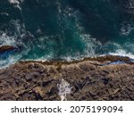 Aerial photograph. Beautiful seascape. Dark turquoise water with white foamy waves and rocky shore. Minimalism. Abstraction. Beauty of nature. Tourism, travel, ecology.