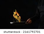 Small photo of The chef cooks rice with shrimps in a frying pan on a black background. Levitation. Sea food recipes, seafood preparation. Recipe book, food blog.