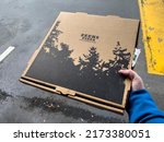 Small photo of Seattle, WA USA - circa May 2022: Close up view of someone holding a Zeek's pizza box in a parking lot.