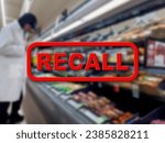 Small photo of Blurred background of a grocery store employee removing recalled product with the red text Recall in the foreground