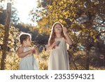 Small photo of Two little girls, sisters outdoors in white dresses, making soap babbles