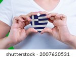 Woman in white t-shirt holds a heart in the form flag Greece on her chest. Photo for a postcard on Flag Day, Independence Day, travel, patriotism, other holiday
