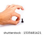 Small photo of Human hand flicking a chess piece, huge hand flicks away a small tiny black pawn. Flick gesture isolated on white. Danger, anxiety and peer pressure, being fired, losing job due to layoffs concept