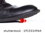 Small photo of Big black boot crushing a small red game piece. Little object pinned down about to be destroyed under a large shoe, closeup Big vs small rich vs poor business social abstract concept, white background