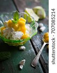 Small photo of Fresh mango and lime syllabub served in a dainty emerald green glass dessert dish garnished with mint and icing sugar on distressed green wooden work surface