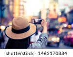 Asian tourist wearing hat is taking pictures with bokeh street lights, a woman wearing a hat, using a photo tablet, Yaowarat Road, beautiful bokeh at Yaowarat Road, Thailand.
