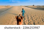 Small photo of Thar desert, Rajasthan, India - 15.10.2019 : Cameleer leading a camel, Camelus dromedarius, into sand dunes.Tourist viewpoint while sitting on camel's back. Camel riding is a favourite sport activity.