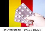 Hand in surgical glove holding pill blisters. Belgian flag in the background